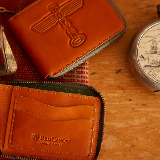 lifestyle image of 2 separate wallets.  one shown unzipped with the card pockets showing and one wallet showing the front.  Both laying on a table.